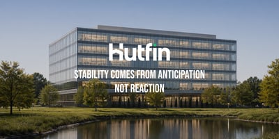 Modern glass office building reflected in a calm water feature, surrounded by landscaped greenery under a clear sky.