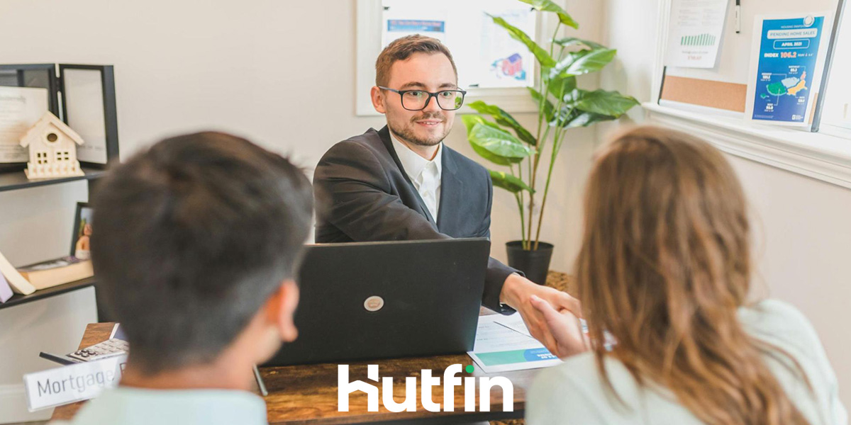 A real estate broker shaking hands with clients across a desk, with the Hutfin logo displayed at the bottom, representing commercial real estate brokerage services.