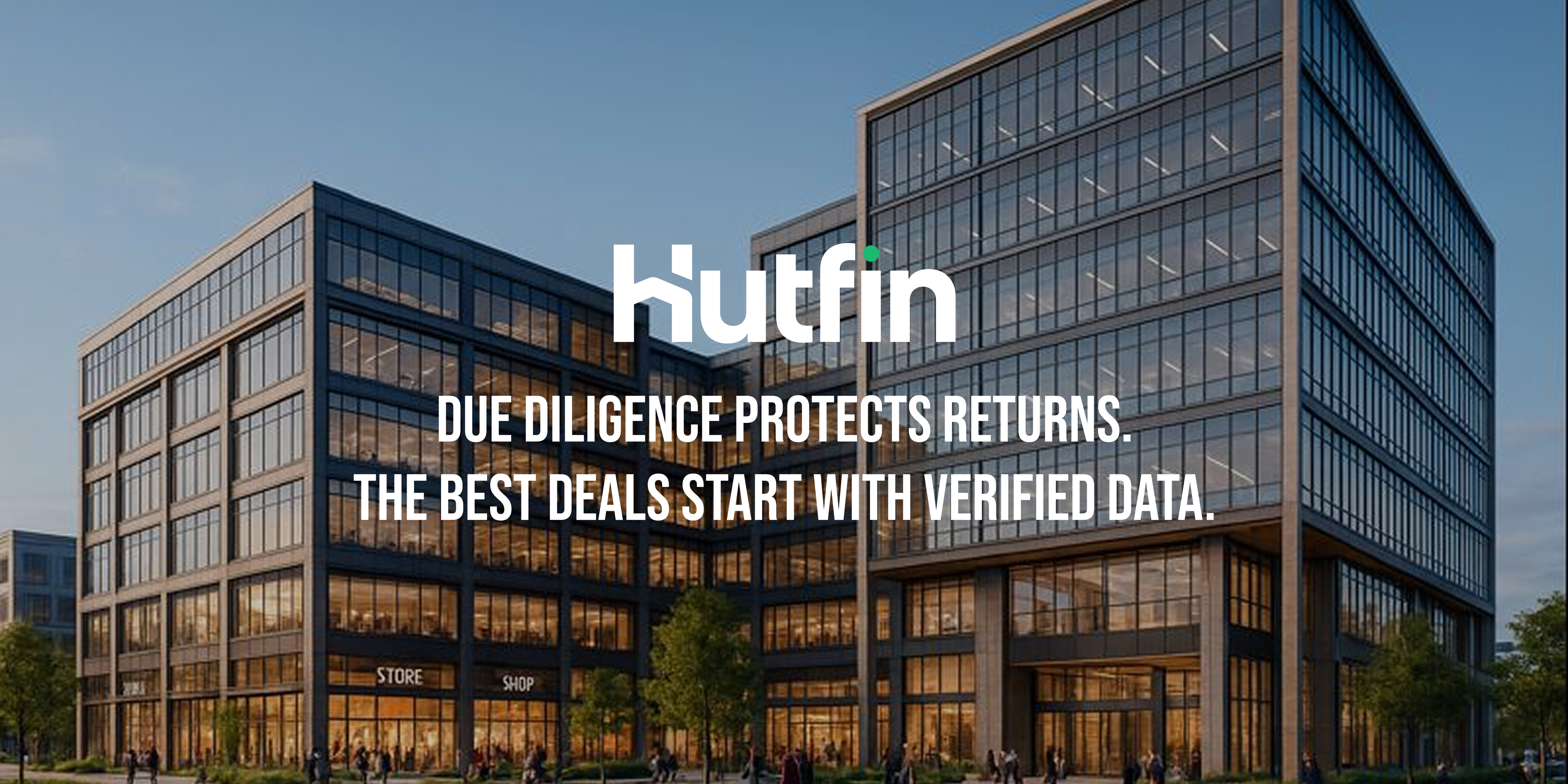 A modern mixed-use commercial building with large glass façades, illuminated interior spaces, and street-level activity, photographed at dusk in an urban setting.